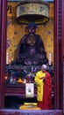 Buddhist monk praying nest to a budha sculpture