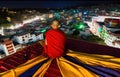 Buddhist monk sits on temple roof and looks at city at night, generative AI