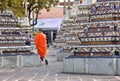 Buddhist monk with traditional orange clothes walking inside of buddha temple between ornaments and mosaic columns in Bangkok, Tha Royalty Free Stock Photo