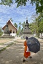 A Buddhist monk with umbrella walks towards the Wat Aham temple of Luang Prabang, Laos Royalty Free Stock Photo