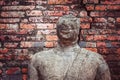 Ayutthaya, Thailand: a crumbling statue with broken-off upper half of the head without eyes on the shabby brick wall background