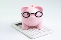 Budget, cost or investment calculation and financial activity concept, pink piggy bank wearing glasses on white calculator on Royalty Free Stock Photo