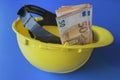 Budget investment in construction. Euro money banknotes and yellow construction helmet. on blue background