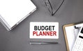 BUDGET PLANNER Text written on the card with notebook and clipboard, grey background