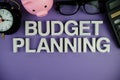 Budget Planning alphabet letters with piggy bank, alarm clock, calculator top view on purple background Royalty Free Stock Photo