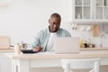 Budget planning concept. Pensive african american man calculating taxes and using laptop computer, sitting in kitchen Royalty Free Stock Photo