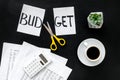Budget reduce concept with accounting, sciccors and paper with cut word budget on black background top view