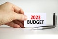 2023 Budget symbol. White card with words 2023 Budget. Businessman hand. Metallic pen. Beautiful white table white background.