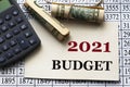 2021 BUDGET - words on white paper against the background of a table of numbers with a calculator and banknotes