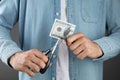 Budgeting. Man cutting dollar banknote with scissors on dark grey background, closeup Royalty Free Stock Photo