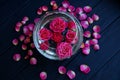 Buds of red roses in water in a glass vase and petals on a table Royalty Free Stock Photo