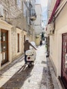 Budva, Montenegro - 17 august 2023: Man in a helmet drives a scooter in his hands along a narrow stone street of an