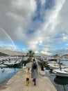 Budva, Montenegro - 25 december 2022: Mom with a little girl walk along the pier against the backdrop of a rainbow over