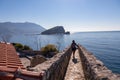 Budva - Tourist woman walking on wall of historical citadel of Budva with Scenic view over Saint Nicholas island