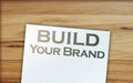 Build Your Own Brand words on a page and paper dollar signs around on wooden table. Branding rebranding marketing