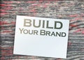 Build Your Own Brand words on a page and paper dollar signs around on wooden table. Branding rebranding marketing
