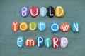 Build your own empire, motivational phrase composed with multi colored stone letters over green sand