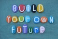 Build your own future, motivational phrase composed with multi colored stone letters over green sand