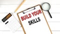 BUILD YOUR SKILLS words on clipboard, with calculator, magnifier and pencil on the white wooden background