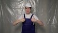 Builder in blue overalls puts on white hard hat and shows thumbs up. Royalty Free Stock Photo