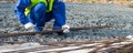 A Builder in a blue uniform, against the background of stones, takes long metal rods for the construction of concrete structures,