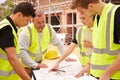 Builder On Building Site Discussing Work With Apprentice