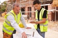 Builder On Building Site Discussing Work With Apprentice