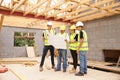 Builder On Building Site Looking At Plans With Apprentices