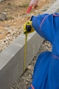 A builder checks the progress of laying curbstone, rubble mounds and takes measurements, close-up