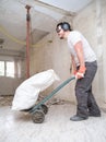 Builder collecting construction debris in a bag, and carrying in a hand trolley