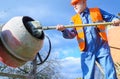 Builder with concrete mixer prepares cement mortar. Construction worker with spade in hand.