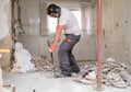 Builder digging up the house floor, lifting up old tiles with a crowbar and a hammer