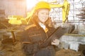 Builder engineer at a construction site, a woman inspector in a helmet and uniform, an excavator digs a pit, earthworks, a Royalty Free Stock Photo