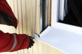 A builder in gloves measures the window outside with a tape measure. Professional craftsman in a red robe with a tool measures Royalty Free Stock Photo