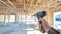 A builder grips a power drill, preparing to work on the interior framework of a construction site filled with wooden beams and a Royalty Free Stock Photo