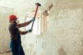 Builder with a hammer in his hands breaks the cement wall The builder is dressed in a protective suit and helmet Royalty Free Stock Photo