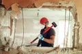 Builder with a hammer in his hands breaks the cement wall The builder is dressed in a protective suit and helmet Royalty Free Stock Photo