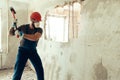 Builder with a hammer in his hands breaks the cement wall The builder is dressed in a protective suit and helmet Royalty Free Stock Photo