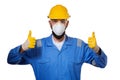 Builder in hard hat in mask and transparent safety glasses raising his thumbs up in working gloves