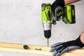 The builder holds in his hand an electric screwdriver on the background of a concrete wall. Screws into a wooden beam. DIY