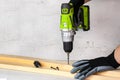 The builder holds in his hand an electric screwdriver on the background of a concrete wall. Screws into a wooden beam. DIY