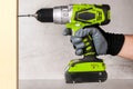 The builder holds in his hand an electric screwdriver on the background of a concrete wall. Screws into a wooden beam. DIY