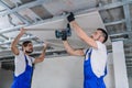 The builder fixes drywall to the ceiling with a drill, his colleague helps him Royalty Free Stock Photo