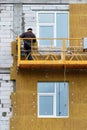 The builder stands on a suspended platform and insulates the facade of a house under construction