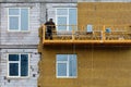 A builder standing on a suspended platform insulates the facade of a high-rise building under construction with mineral