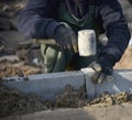 A builder knocks a hammer on a cement block, sets concrete curbs in the cement.