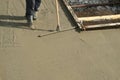 Builder mason worker leveling concrete with long trowel on construction site.