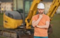 Builder near excavator. Builder worker with excavator. Builder in helmet. Worker in hardhat. Portrait mechanical worker