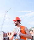 Builder orange vest and helmet works at construction site. Contractor control according to plan. Guy protective helmet