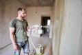 Builder is painting with airbrush wall, house repairment. Large volume of work is visible in the background